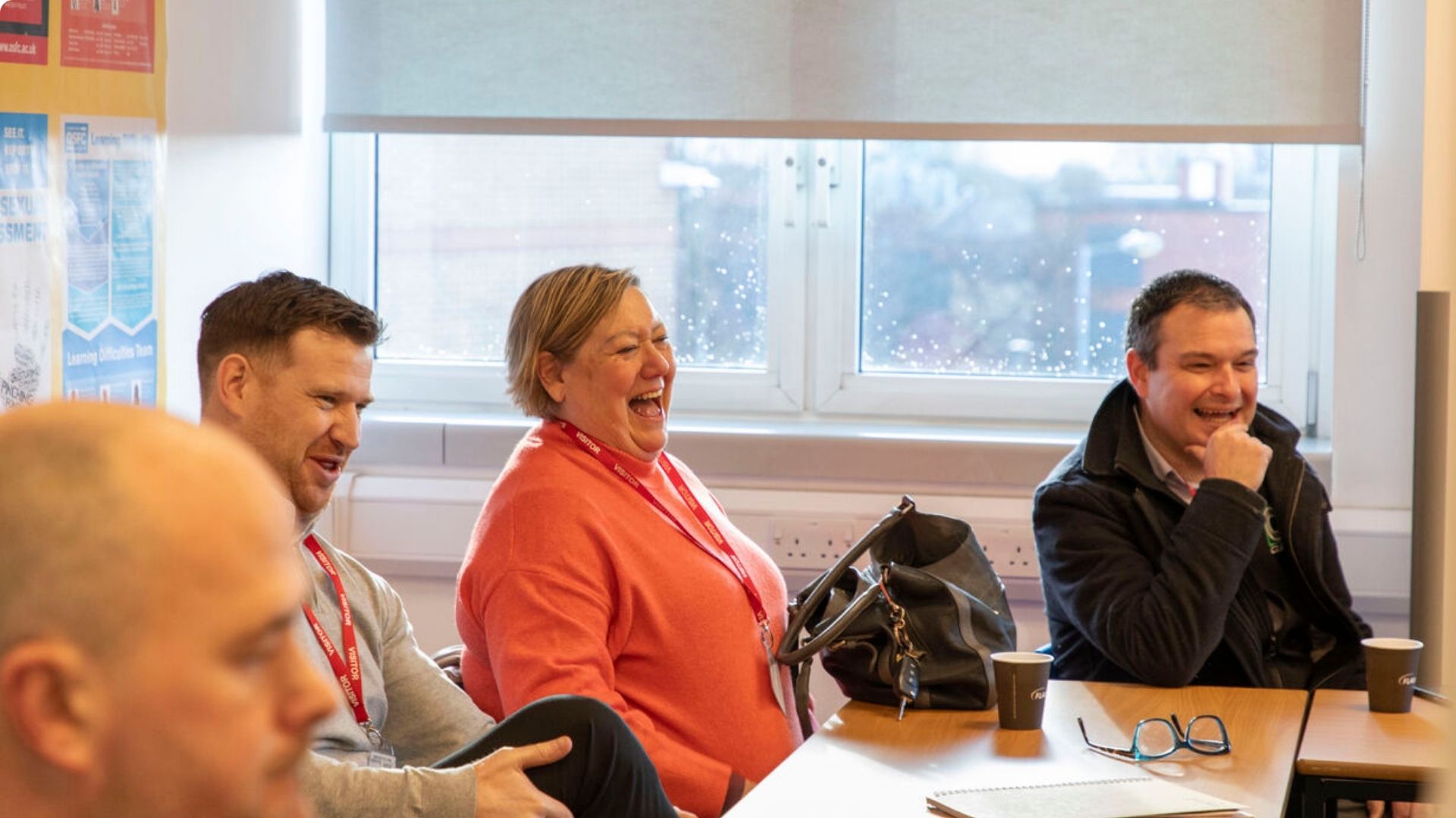 Group of people, sitting on desks, laughing and talking, looking optimistic and cheerful